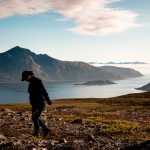 Nainen patikoimassa, taustalla vuoria ja vuono.