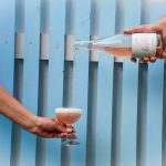 Käsi kaataa viiniä lasiin, taustalla sininen seinä