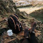 Reppu, kahvikuppi ja jalat kallion rinteellä