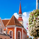 Kirkko ja rakennuksia kesäisenä päivänä, edustalla kukka-amppeli.