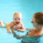 Äiti pitelee nauravaa vauvaa käsivarsillaan altaassa.