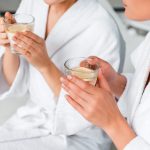 Kaksi naista nauttii lämmintä sitruunavettä kylpytakit päällään.