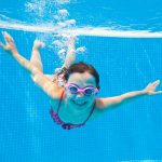 Tyttö sukeltaa ja hymyilee kameralle veden alla.