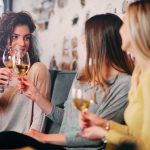 Kolme naista keskustelee baarissa viinilasit kädessään.