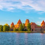 Trakain linna heijastuu vedestä, saaren reunalla kuumailmapallo.