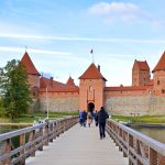 Ihmisiä kulkee puista siltaa pitkin kohti linnaa.