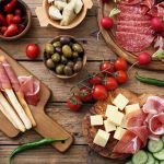 Leikkeleitä, juustoja, oliiveja, tomaatteja ym. antipastolajitelmassa puisella pöydällä.