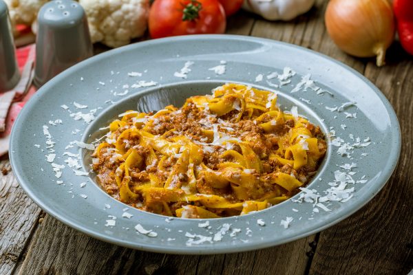 Tagliatelle-nauhapastaa bolognesekastikkeella lautasella, pinnalla juustoraastetta.