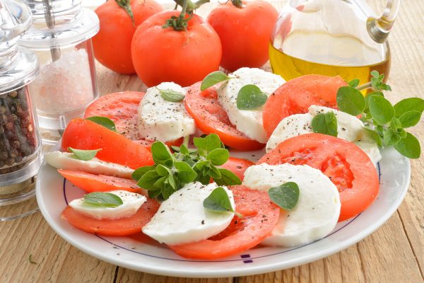 Tomaattia, mozzarellajuustoa ja basilikaa lautasella, taustalla maustesirottimet ja oliiviöljykannu.