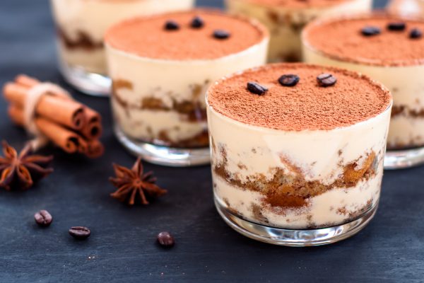 Tiramisuannoksia lasiastioissa, vierellä mausteita ja kahvipapuja.