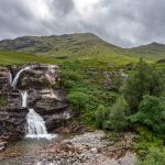 Vesiputous vuorten juurella pilvisenä päivänä.