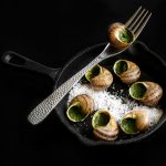 Maustettuja etanoita pannulla, haarukka ja suolakiteitä.