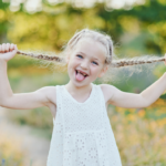 Pikkutyttö kesällä ulkona mekossa, pitelee lettejään ja ilmeilee.