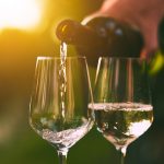 Käsi kaataa pullosta valkoviiniä laseihin