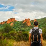 Mies katselee punaisia kalliomuodostelmia reppu selässään.