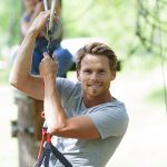 Hymyilevä mies etenemässä ilmaköysiradalla.