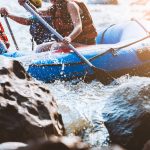 Ryhmä melomassa kumilautalla koskessa kivien keskellä.