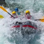 Laskijoita koskessa kumiveneessä vesipärskeiden keskellä.