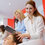 Hymyilevä nuori nainen tekemässä päähierontaa asiakkaalle kampaamossa.