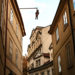 Katutaideteos kujalla, patsas roikkuu kattoparrussa kadun yllä.