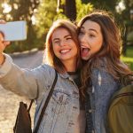 Kaksi farkkutakkeihin pukeutunutta tyttöä ottaa syyspäivänä selfietä.