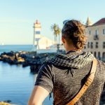 Mies katselee rannalta merelle, taustalla majakka ja vanha kivitalo.