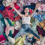 Nuori nainen makoilee vaatteiden peittämällä lattialla riemukas ilme kasvoillaan.