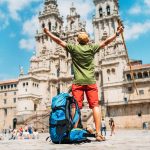 Vaeltaja kohottaa käsiään ilmaan aukiolla historiallisen rakennuksen edessä.