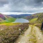 Vaeltaja laskeutuu polkua pitkin kohti järveä Skotlannin karuissa vuoristomaisemissa.