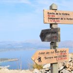 Puinen vaellusreittikyltti, taustalla meri ja vuoristoa.