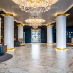 Hotellin aula/vastaanotto, koristeelliset pylväät ja kattolamppu, nojatuolit, sohva