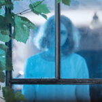 Valkoisiin pukeutunut tyttö katselee ikkunan takana