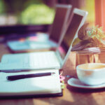 Läppäri ja muistiinpanovälineet kahvilan pöydällä