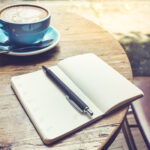 Kirjoituslehtiö ja kahvikuppi on aseteltu pöydälle.