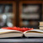 Pöydällä makaa avoin kirja ja sulkakynä.