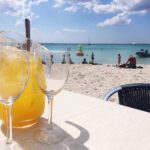 Kannullinen kylmää mehua ja kaksi lasia pöydällä uimarannalla.