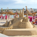 Suuri hiekkalinna rannalla aurinkovarjojen edustalla.