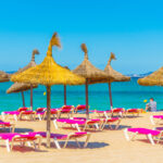 Aurinkotuoleja ja varjoja rannalla.