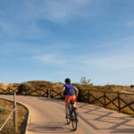 Pyörälijä polkee loivaa ylämäkeä aidatulla kadulla tyhjän maaston keskellä.