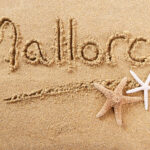 Mallorca kirjoitettuna hiekkaan, alapuolella kaksi meritähteä.