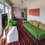 huone, jossa vihreä sohva, sohvapöytä ja tv, taustalla tuoleja ja sängynpääty