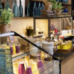 aamiaistarjoilu, smoothie kannuja,lautasia ja tyhjiä värikkäitä koristelasipulloja hyllyllä