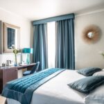 hotellihuone, jossa sänky ja kirjoituspöytä sinisellä päiväpeitteellä ja koristetyynyillä