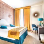 Hotellihuone parivuoteella, jossa keltainen päiväpeite ja siniset koristetyynyt