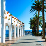 Valkoisia kivikaaria ja palmuja aukiolla, taustalla meri.