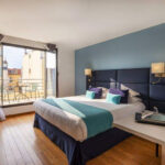 Hotellihuone, jossa turkoosi sisustus ja ovet auki parvekkeelle