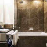 Kylpyhuone jossa tumma marmoriseinä, kylpyamme ja lavuaari