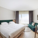 Hotellihuone parivuoteella ja vihreällä sohvalla.